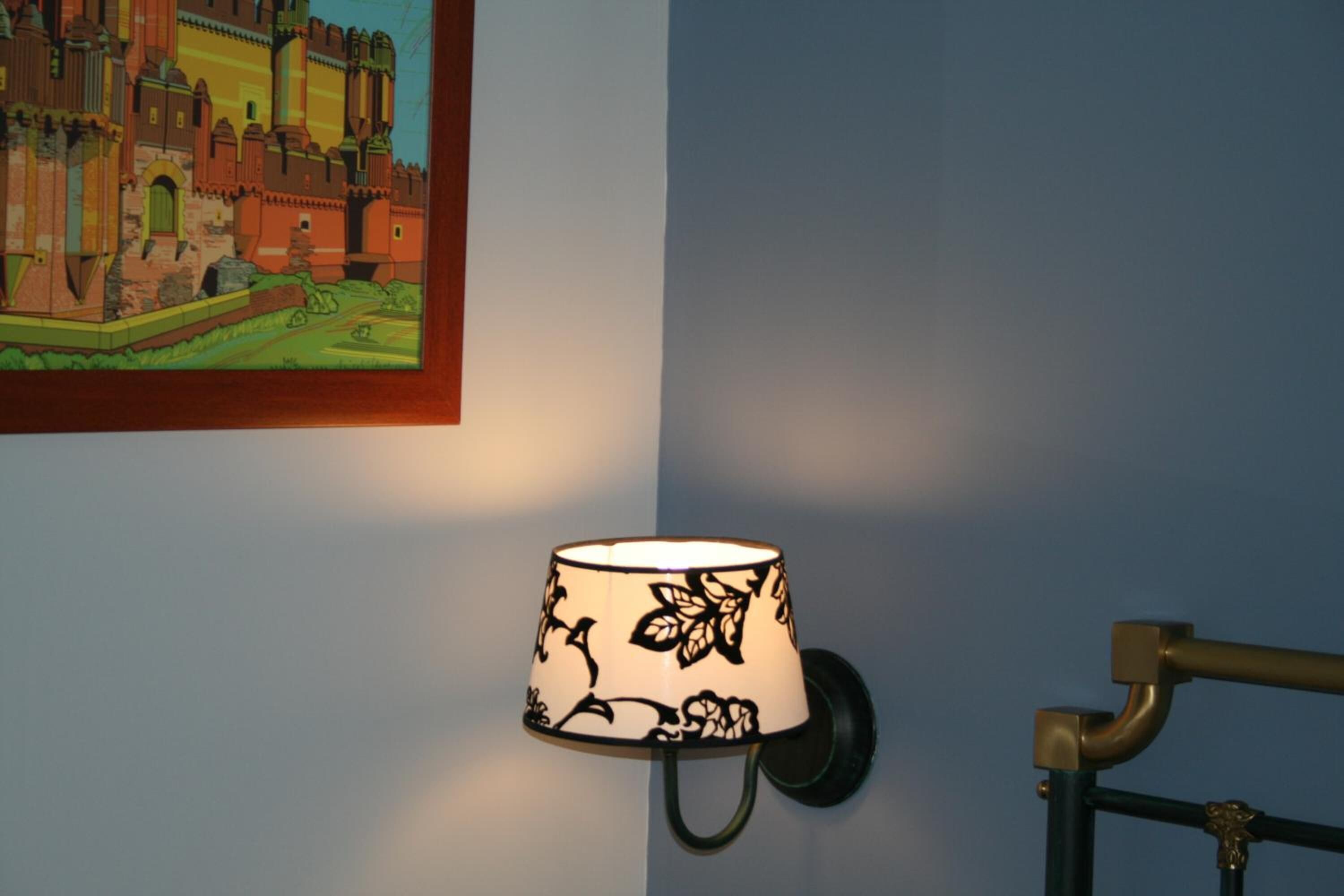 Une lampe murale ornée de motifs floraux, une illustration encadrée représentant un château et une rambarde métallique de couleur sombre.