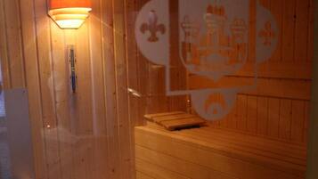 Eine Holzsauna mit Bänken, einem Wandofen und einer kleinen Holzbank am Eingang.