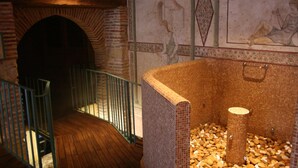 Una habitación con chimenea de ladrillo, detalles decorativos de mosaicos en la pared y suelo de baldosas.