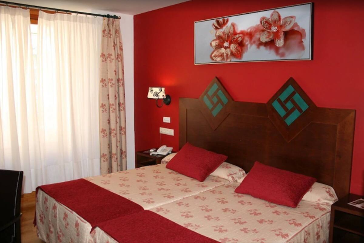 Ein Hotelzimmer mit Bett, roten Wänden, einem Blumenbild und einem hölzernen Kopfteil.