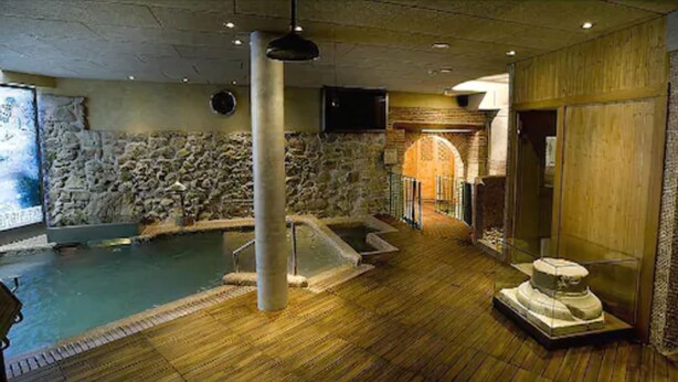 Un área de spa con pared de piedra, suelo de madera, bañera de hidromasaje y camilla de masaje.