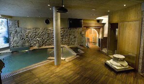 A spa area with a stone wall, a wooden floor, a hot tub, and a massage table. - Hotel Spa La Casa Mudéjar (Segovia)