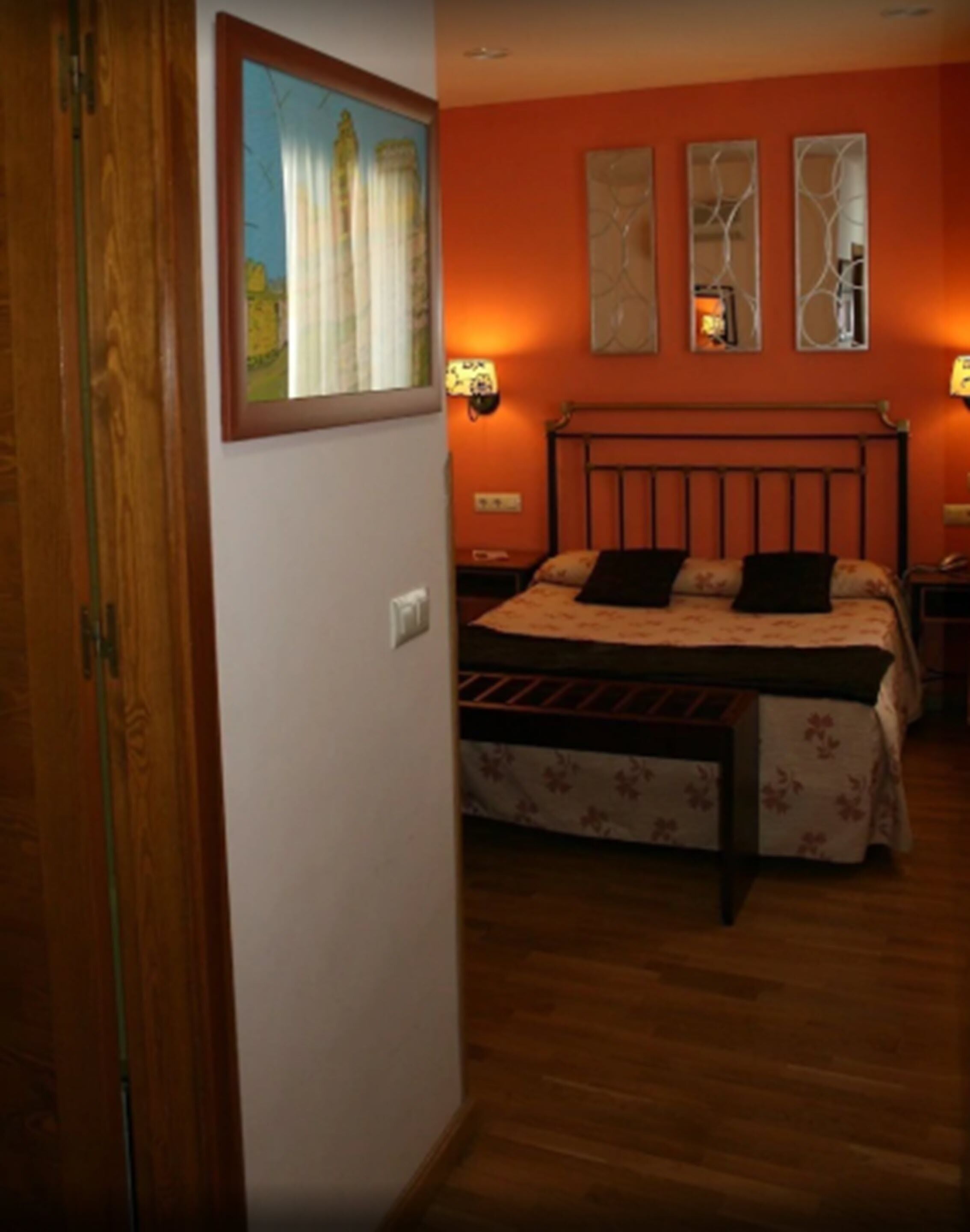 Un dormitori amb un llit de fusta, un quadre a la paret i dues làmpades penjades.