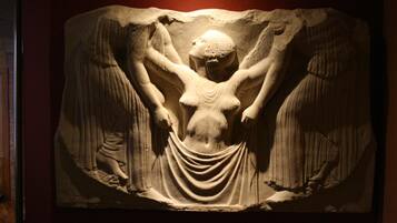 Una escultura de mármol con una figura central rodeada de alas, sobre un fondo oscuro.