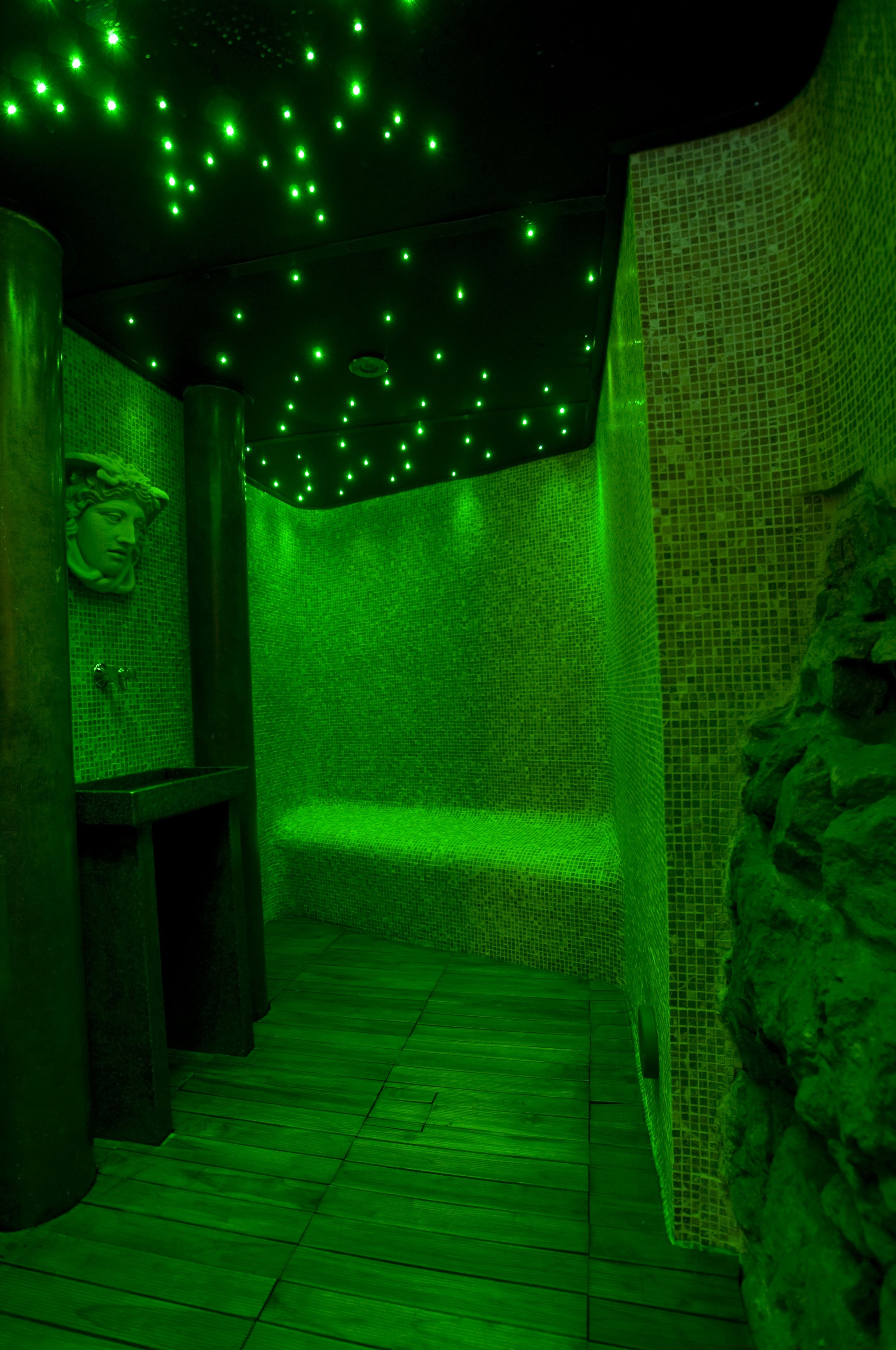 A room with a green-lit ceiling, a stone wall, and a wooden floor.