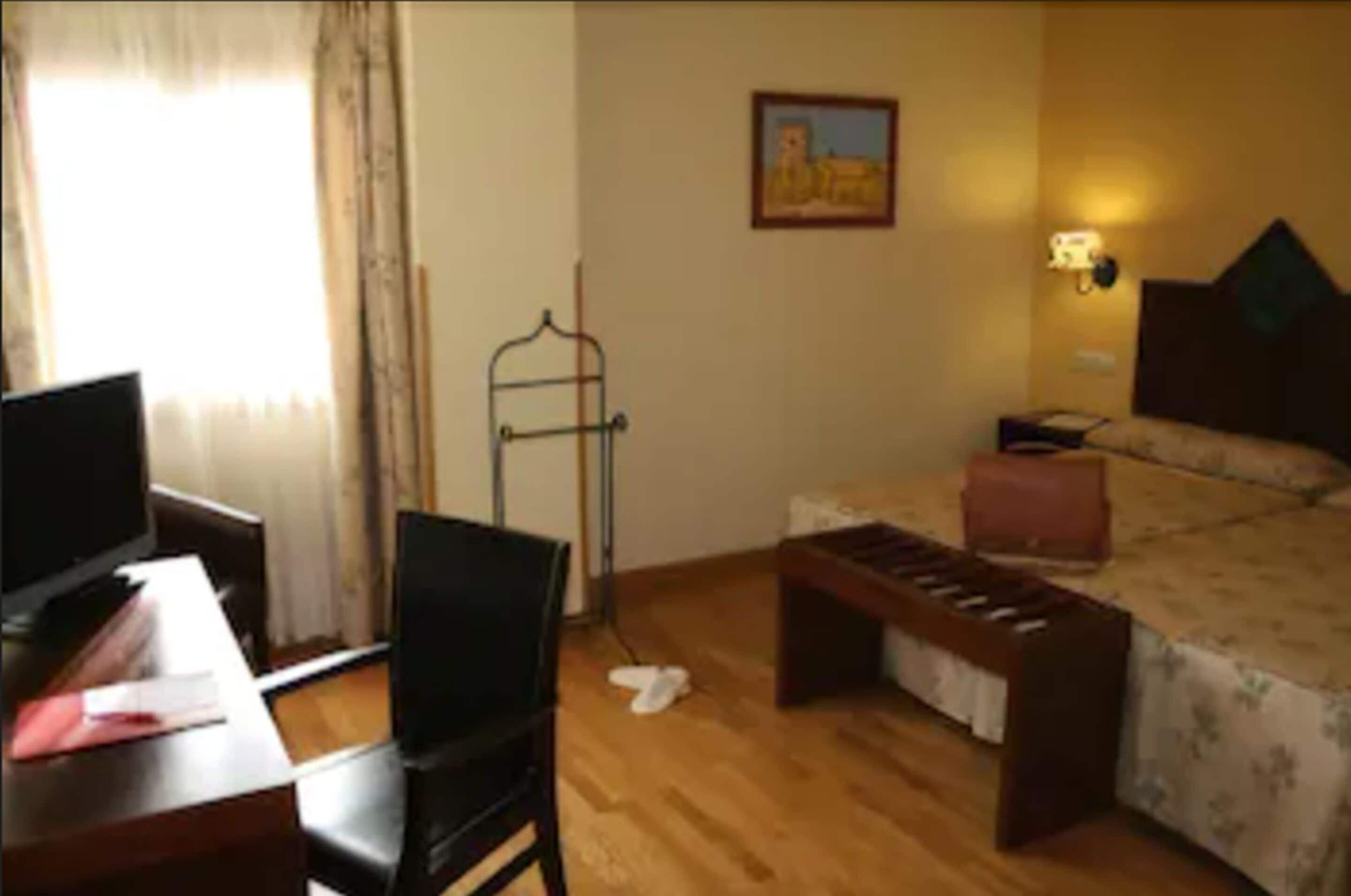 A hotel room with a bed, a desk with a computer, a chair, and a window with curtains.