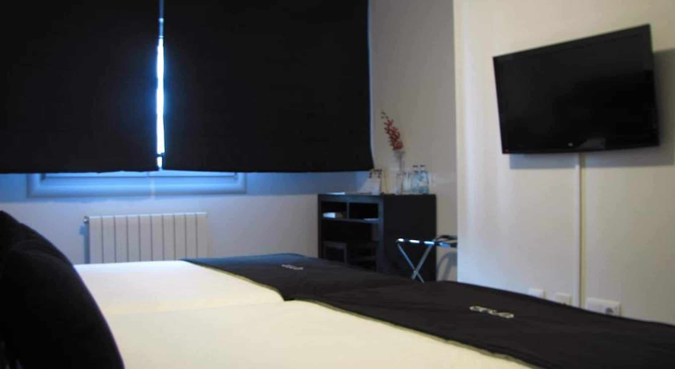 A hotel room with a bed, a television on the wall, and a window with blinds.