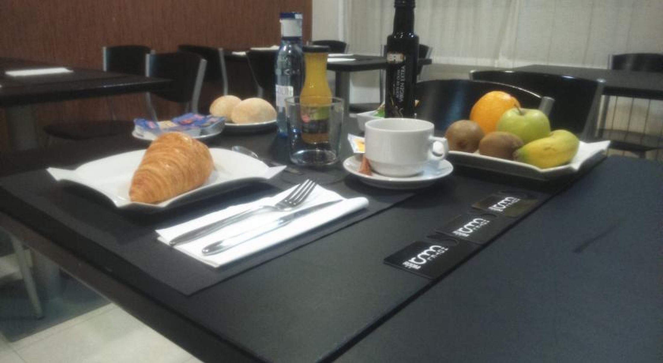 Bandeja de desayuno con croissant, fruta y una taza de café sobre una mesa de hotel.