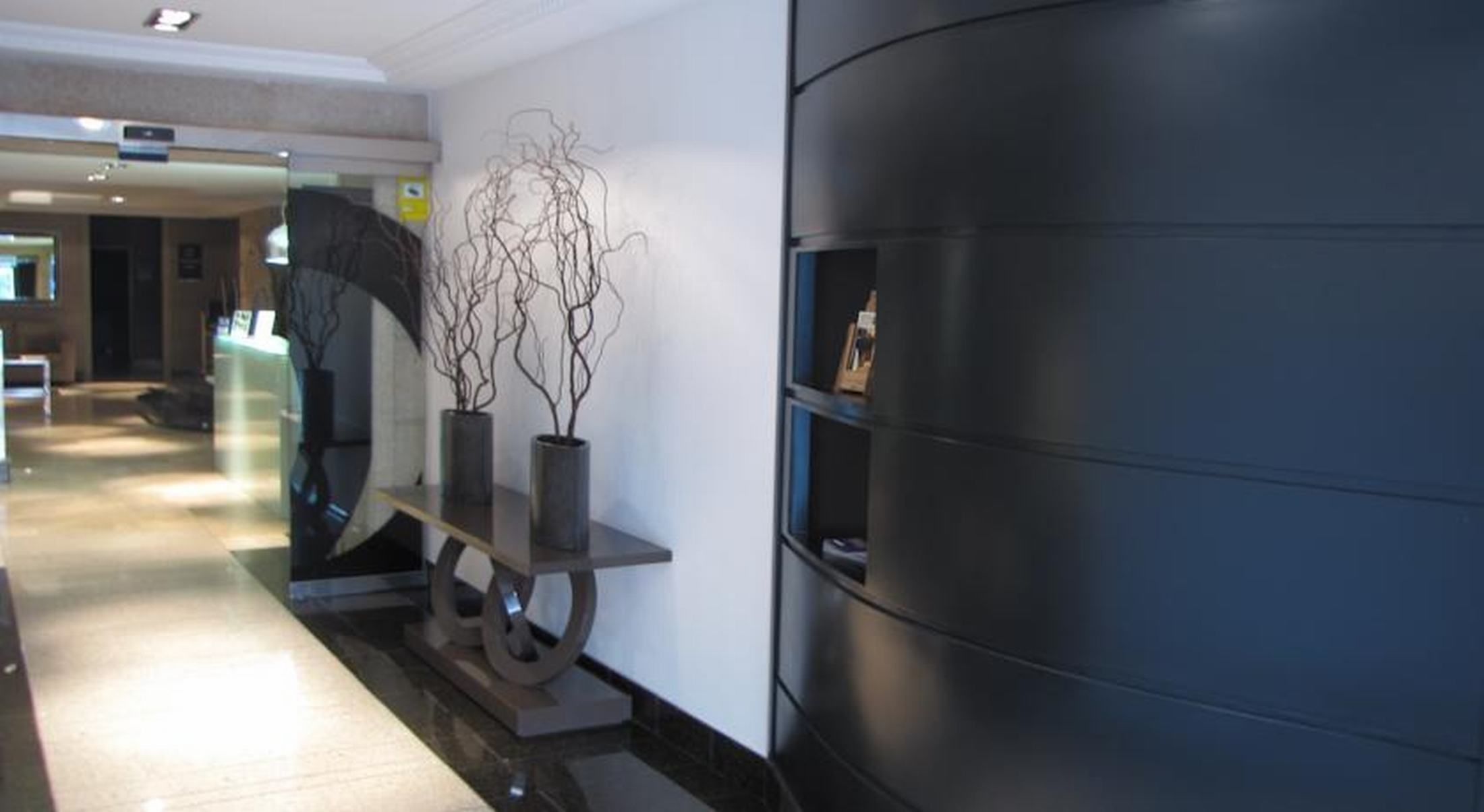 A hallway with a reception desk, a wall-mounted sculpture, and a dark-colored wall with a shelf.