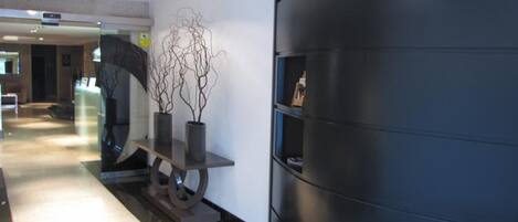 A hallway with a reception desk, a wall-mounted sculpture, and a dark-colored wall with a shelf.