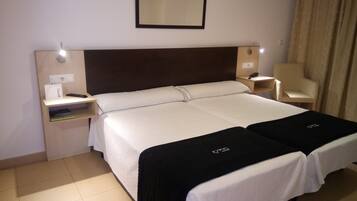 Ein Hotelzimmer mit Doppelbett, Nachttischen, einem Sessel und einem Schreibtisch mit Telefon und Lampe.