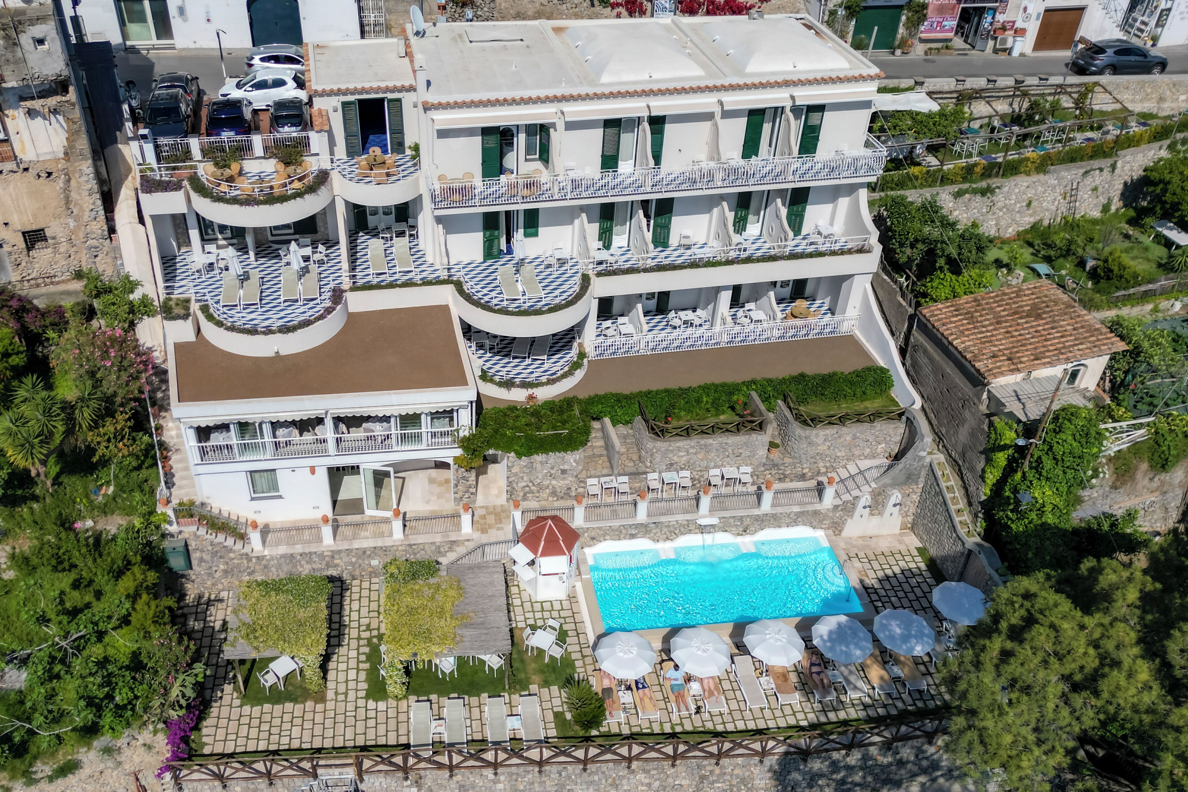 Um hotel de vários andares com piscina no terraço, área de estar ao ar livre e um jardim paisagístico.