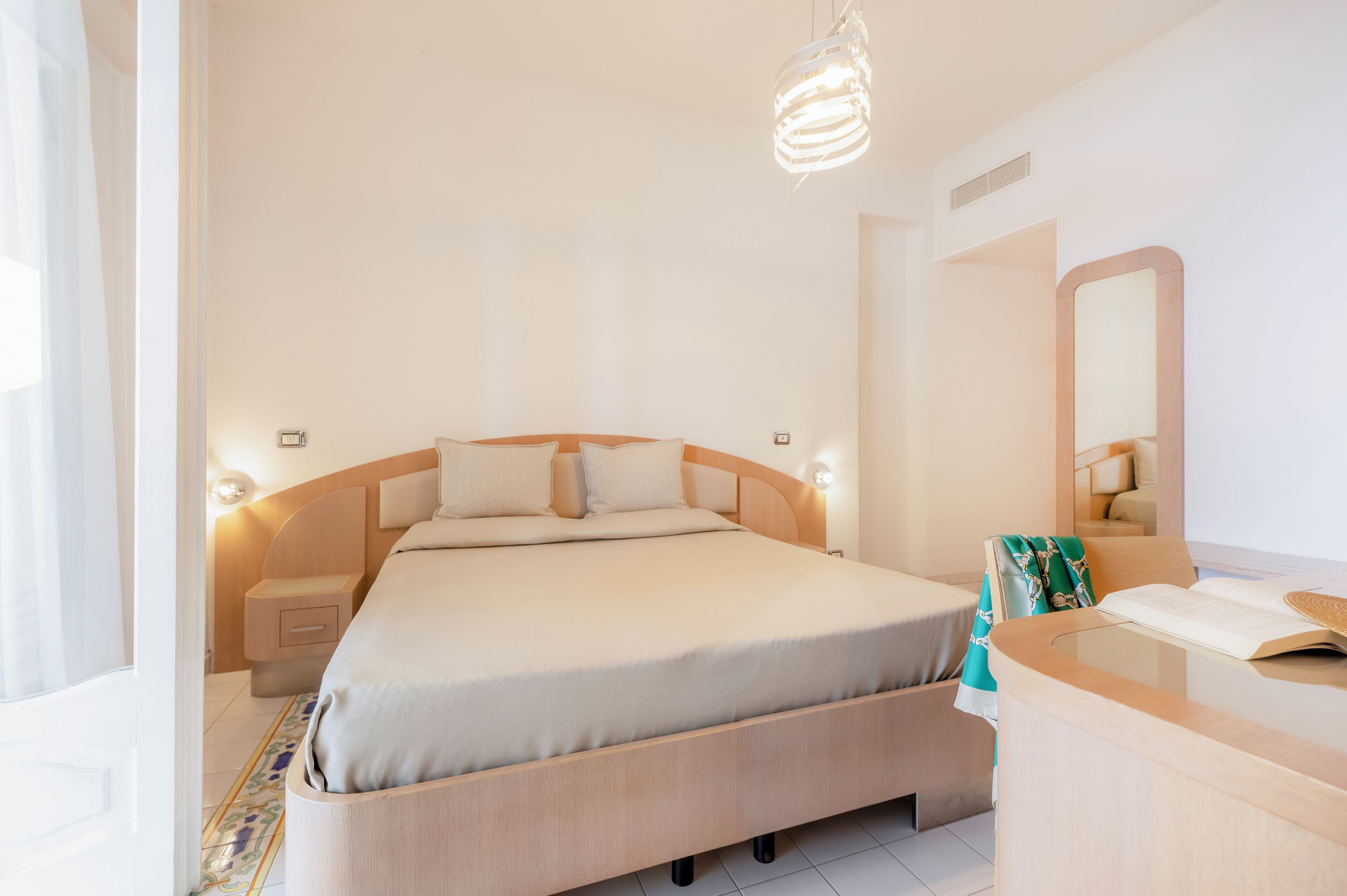 A modern bedroom with a bed, bedside tables, a nightstand, a mirror, and a reading area with a book and a magazine.