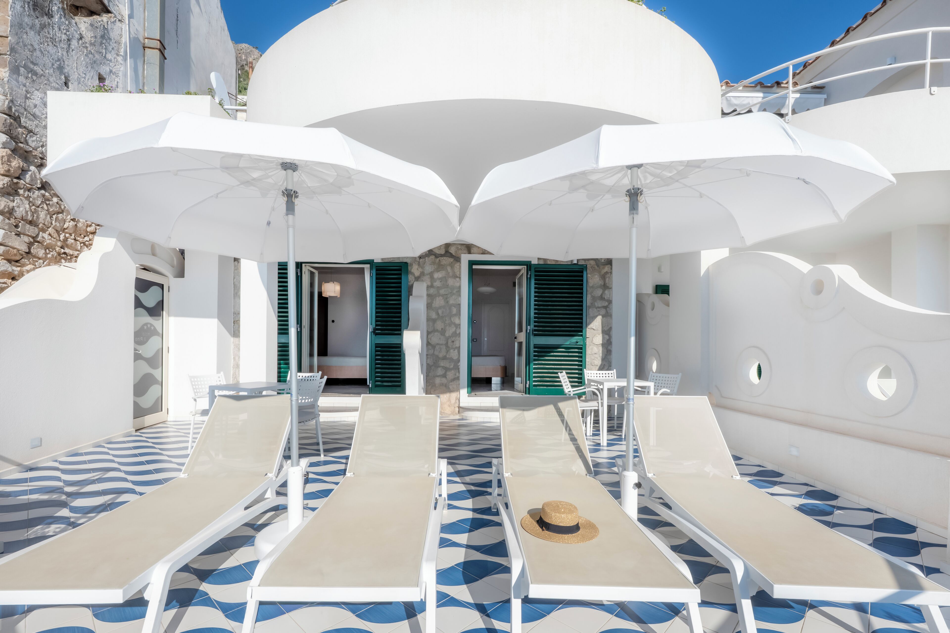 Un espace de détente extérieur, baigné de lumière, avec des parasols blancs, des chaises longues et un sol à motifs.