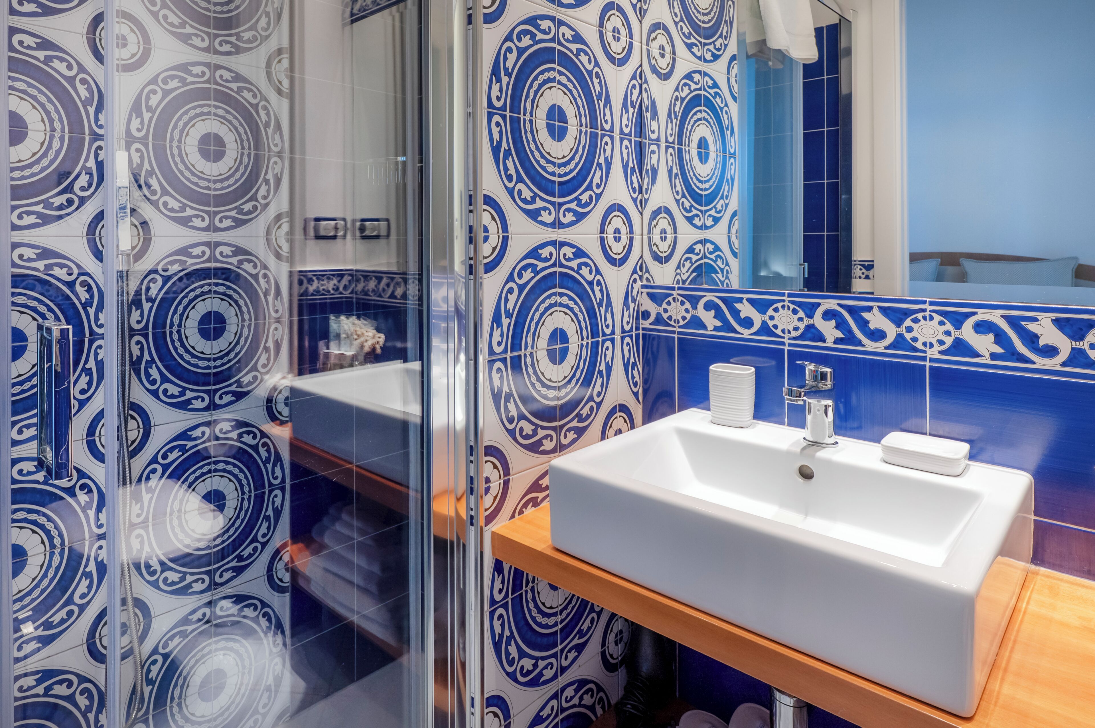 A bathroom with a white sink, blue and white patterned tiles, and a glass shower enclosure.