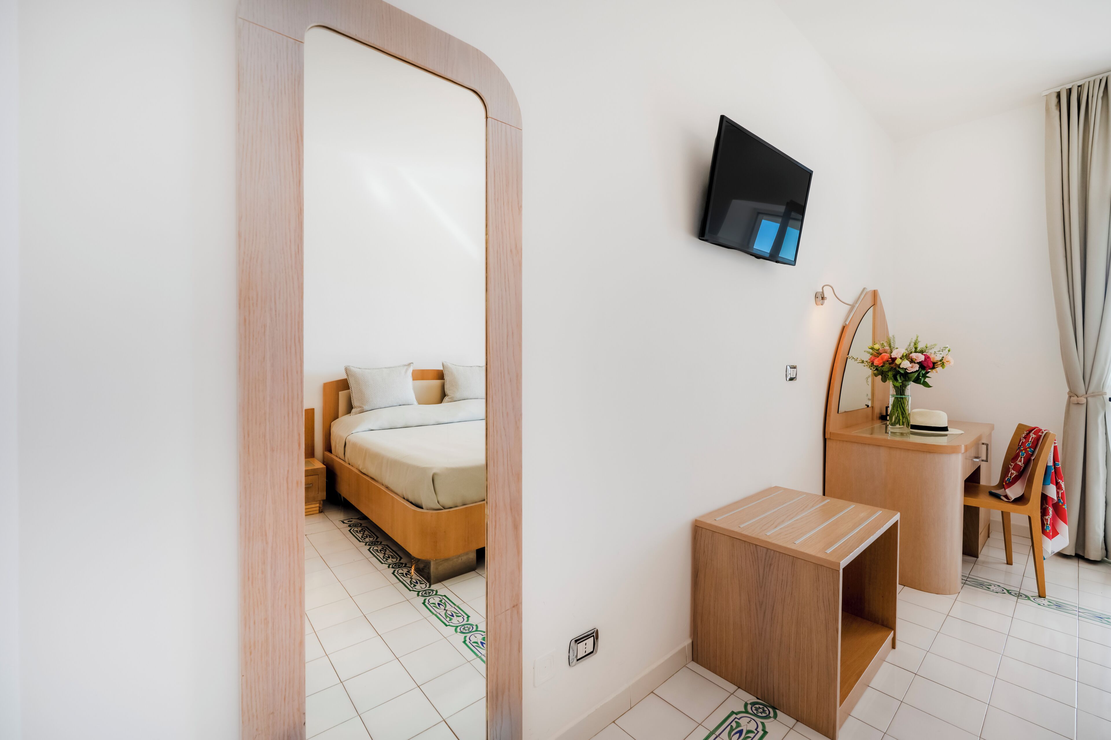 Una habitación de hotel moderna con una cama, un televisor montado en la pared, una pequeña mesa de madera y un espejo.