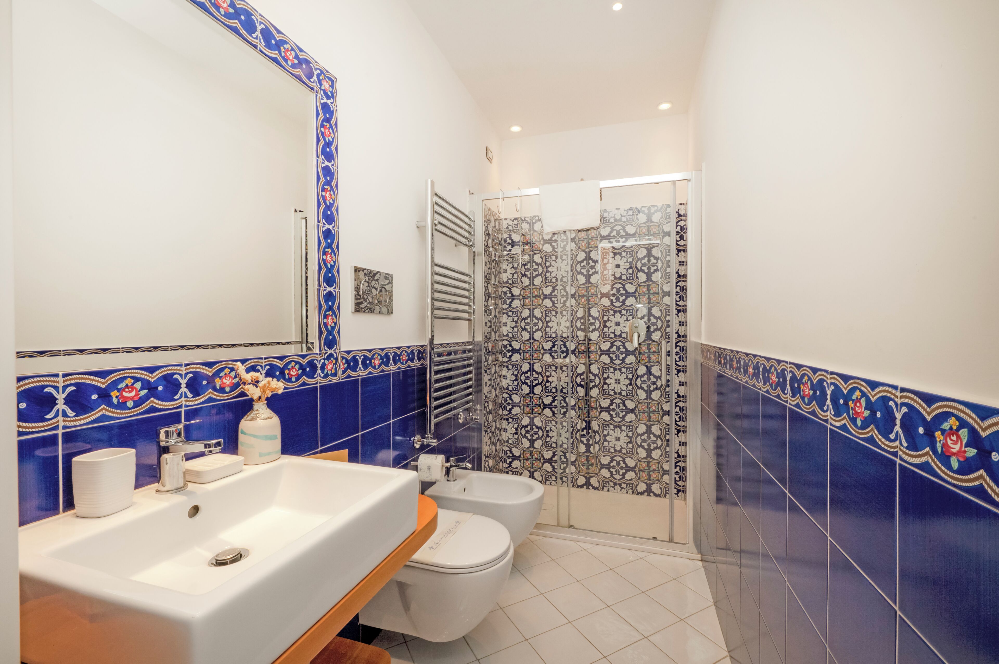 Ein Badezimmer mit Waschbecken, zwei Toiletten, einer Dusche und blauen Dekorfliesen.