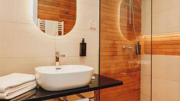 Un baño moderno con ducha de vidrio, un espejo redondo y un lavamanos blanco.