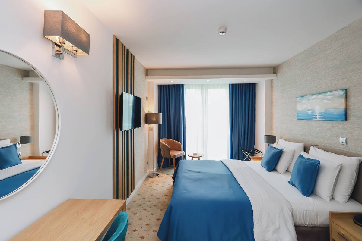 A hotel room with a large bed, a desk, a chair, a TV, and a painting on the wall.