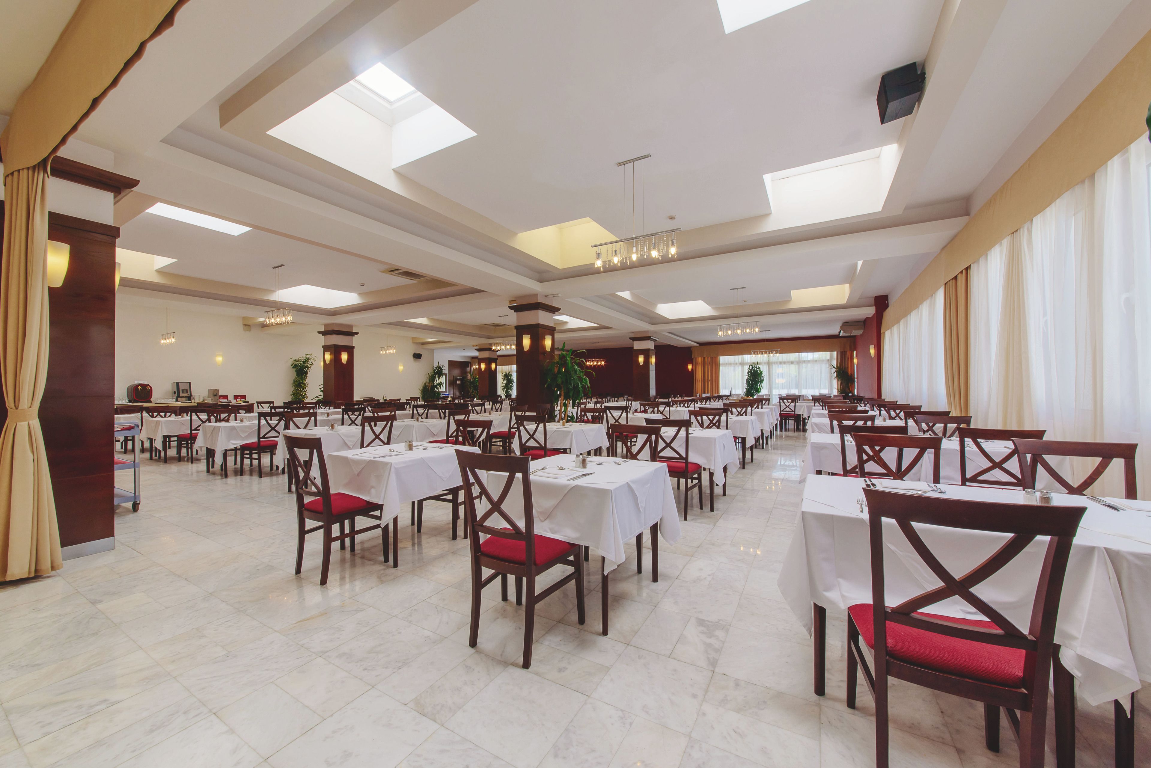 A spacious banquet hall with multiple tables and chairs, high ceilings with skylights, and a clean, modern design.