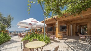 An outdoor patio with wicker chairs and tables, umbrellas, and a view of the sea. - Hotel Montenegro Beach Resort (Becici)