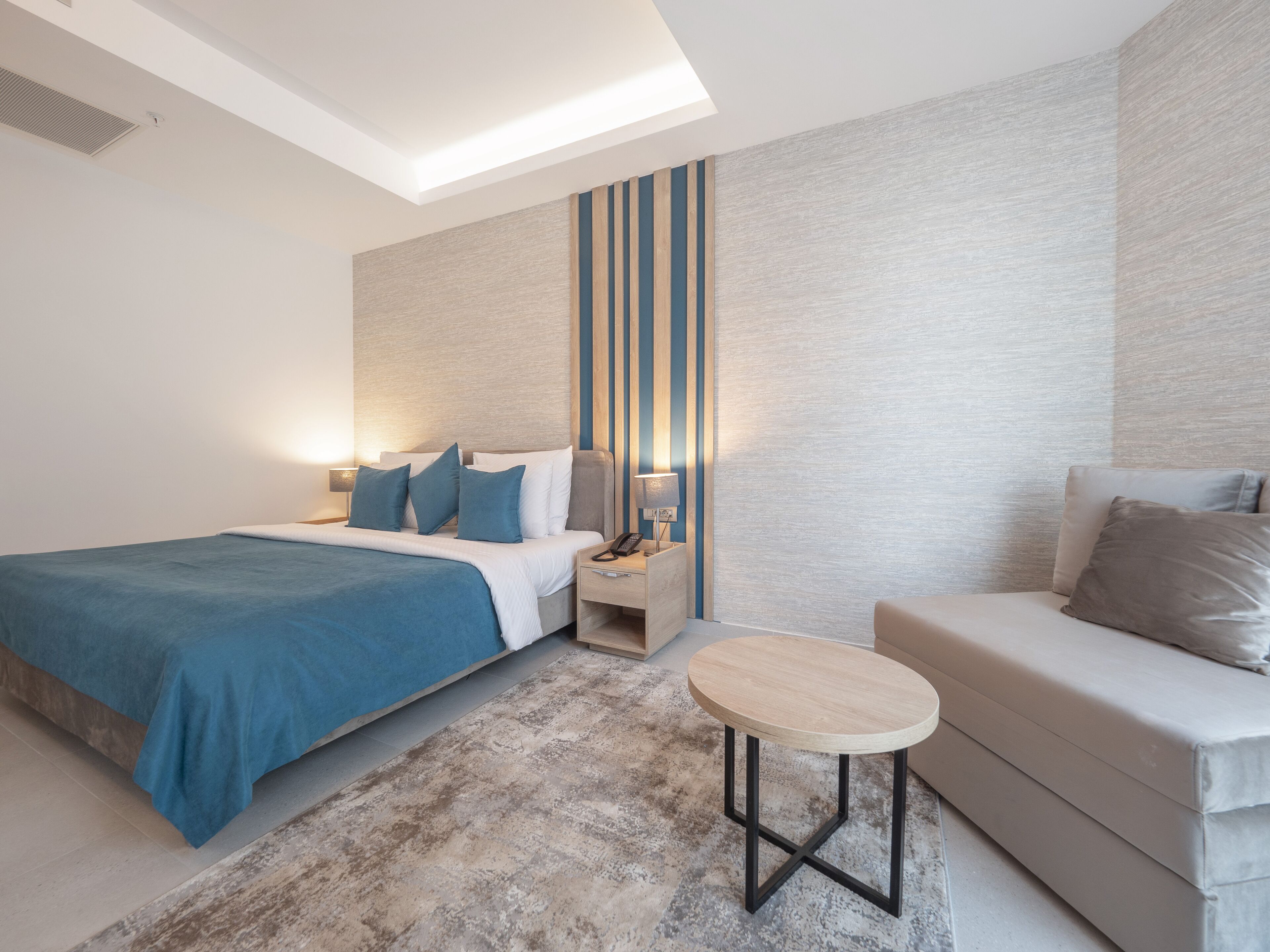 Une chambre d’hôtel moderne avec un grand lit, un canapé, une petite table et une table de chevet avec une lampe.