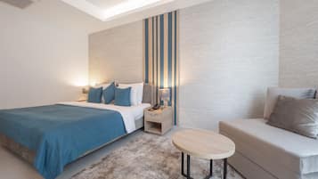 A modern hotel room with a large bed, a sofa, a small table, and a nightstand with a lamp.