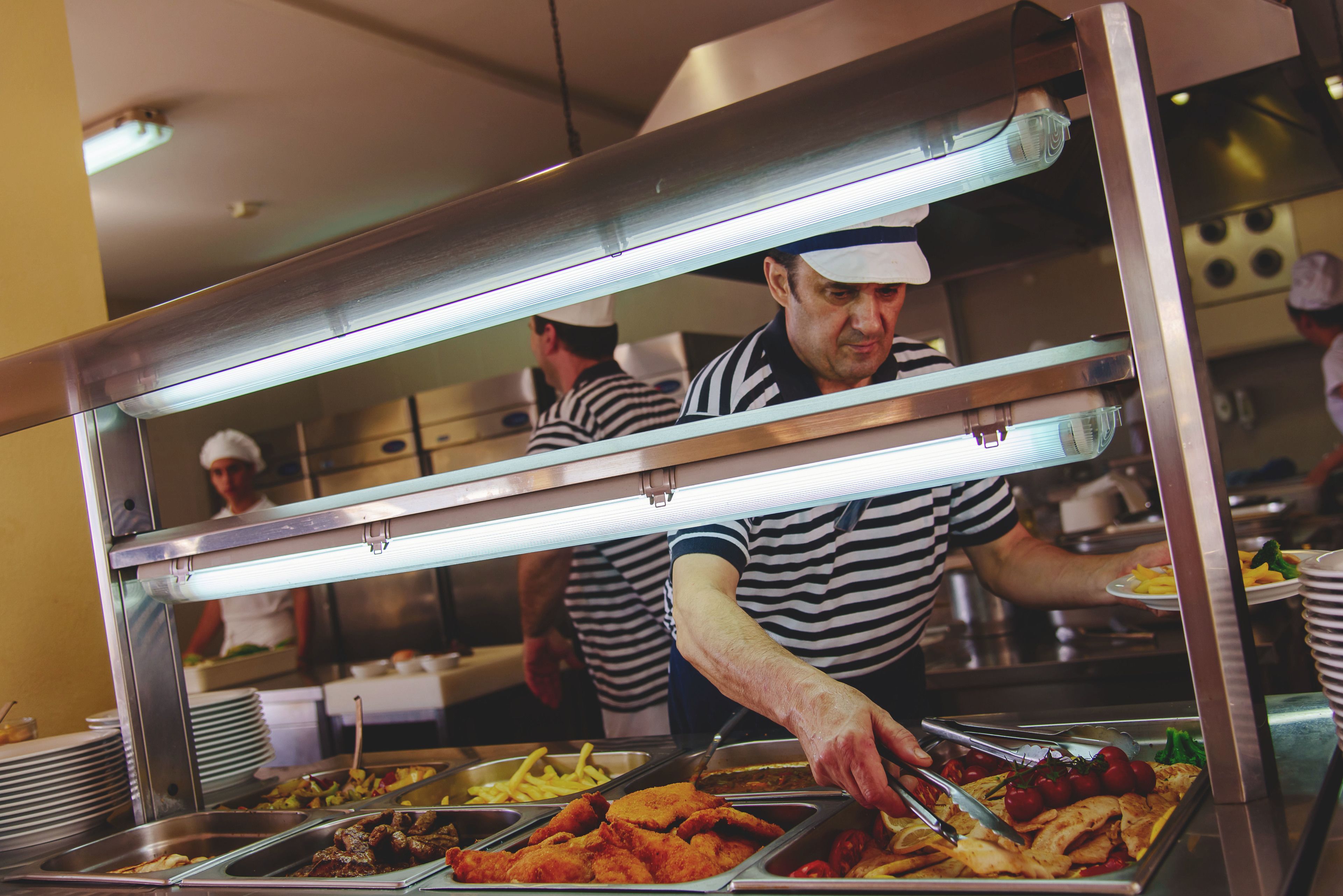 A buffet setup with various food items and a person serving.
