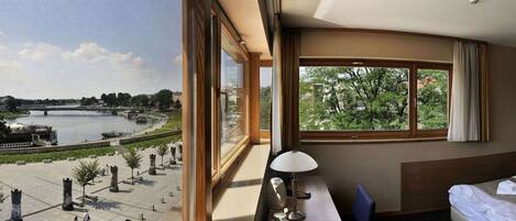 Habitación de hotel con un ventanal grande que ofrece vistas a un paseo fluvial y un puente.