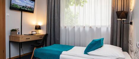 Habitación de hotel con cama, escritorio con computadora, televisor montado en la pared y ventana con cortinas.