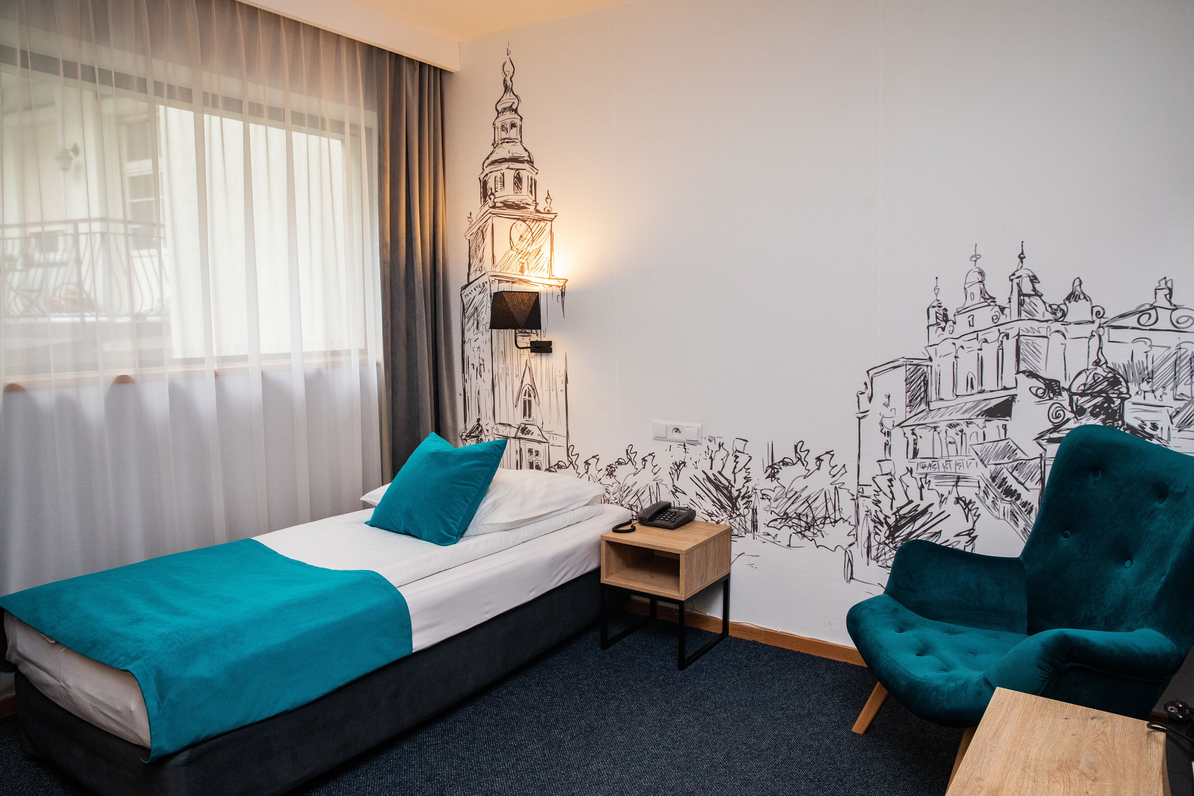 A hotel room with a bed, a nightstand, a chair, and a wall mural of a cityscape.