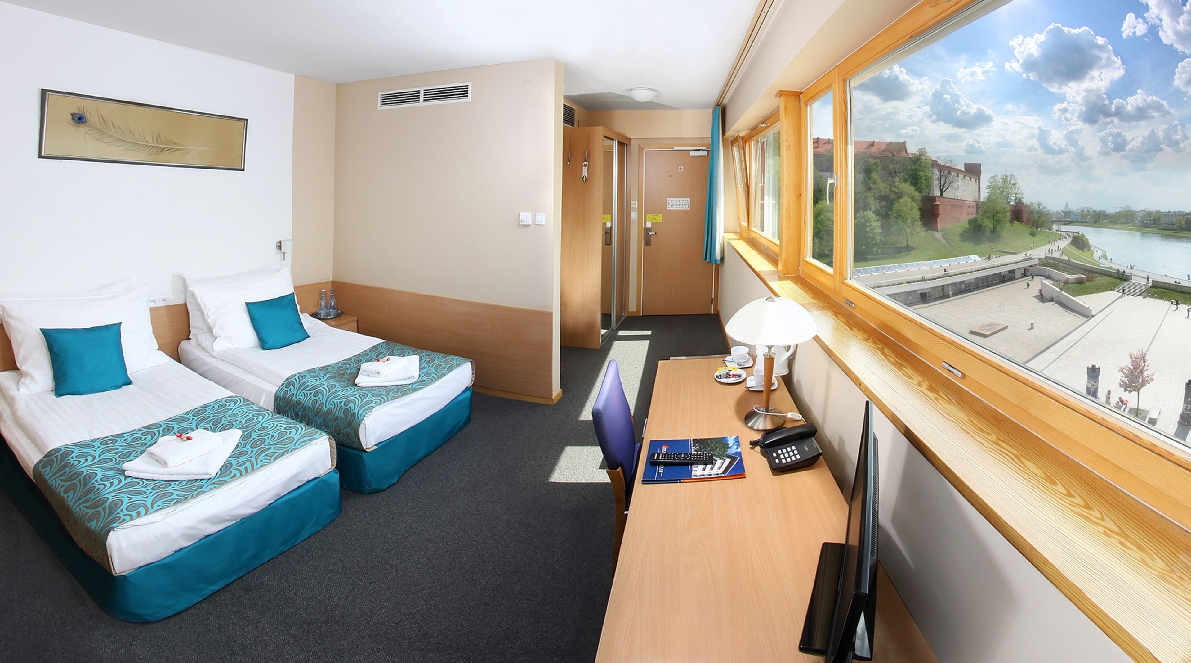 A hotel room with two beds, a desk, a TV, and a window with a view of a cityscape.