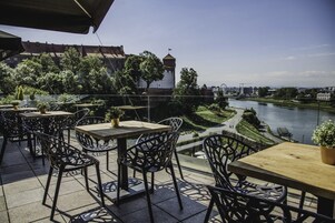 An outdoor terrace with tables and chairs, overlooking a river and a historic building.