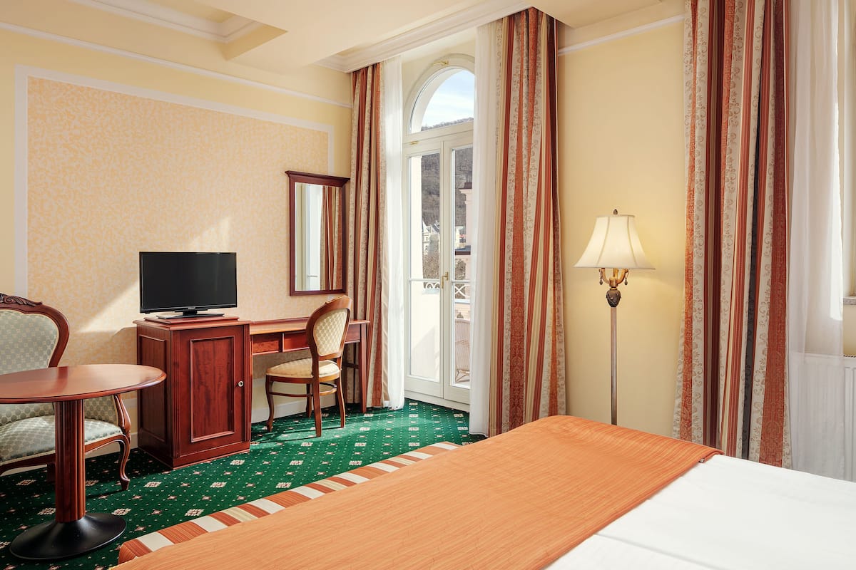 Una habitación de hotel con cama, escritorio, televisor, silla y lámpara.