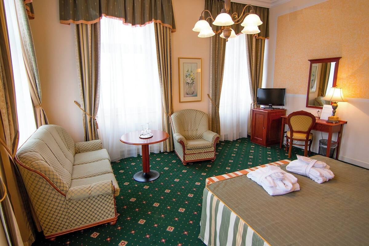 Una habitación de hotel con una cama, dos sillas, una mesita, un televisor y una lámpara.