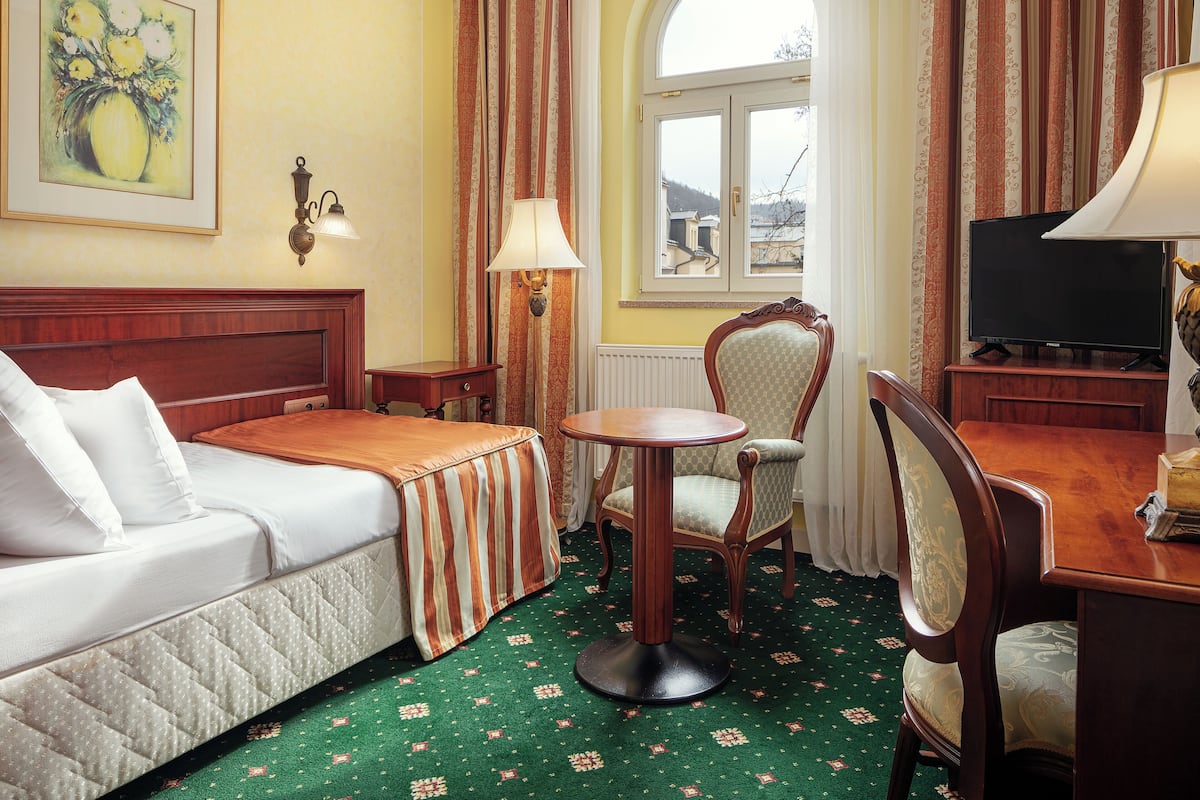 Habitación de hotel con cama, una mesa redonda, una silla, televisión y ventana con cortinas.