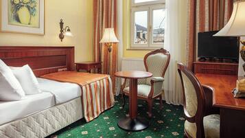 A hotel room with a bed, a round table, a chair, a television, and a window with curtains.