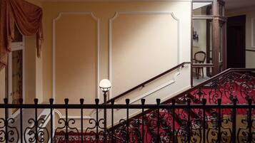 Una escalera con barandillas negras ornamentadas, una alfombra roja y una pared color beige con molduras decorativas.