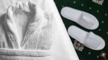 A white bathrobe and white slippers on a bed with a green patterned bedspread.