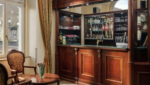 Eine Bar mit Holzausbau, Regalen für Gläser und Flaschen, einem kleinen Tisch mit Stühlen und einem Fenster mit Vorhängen.