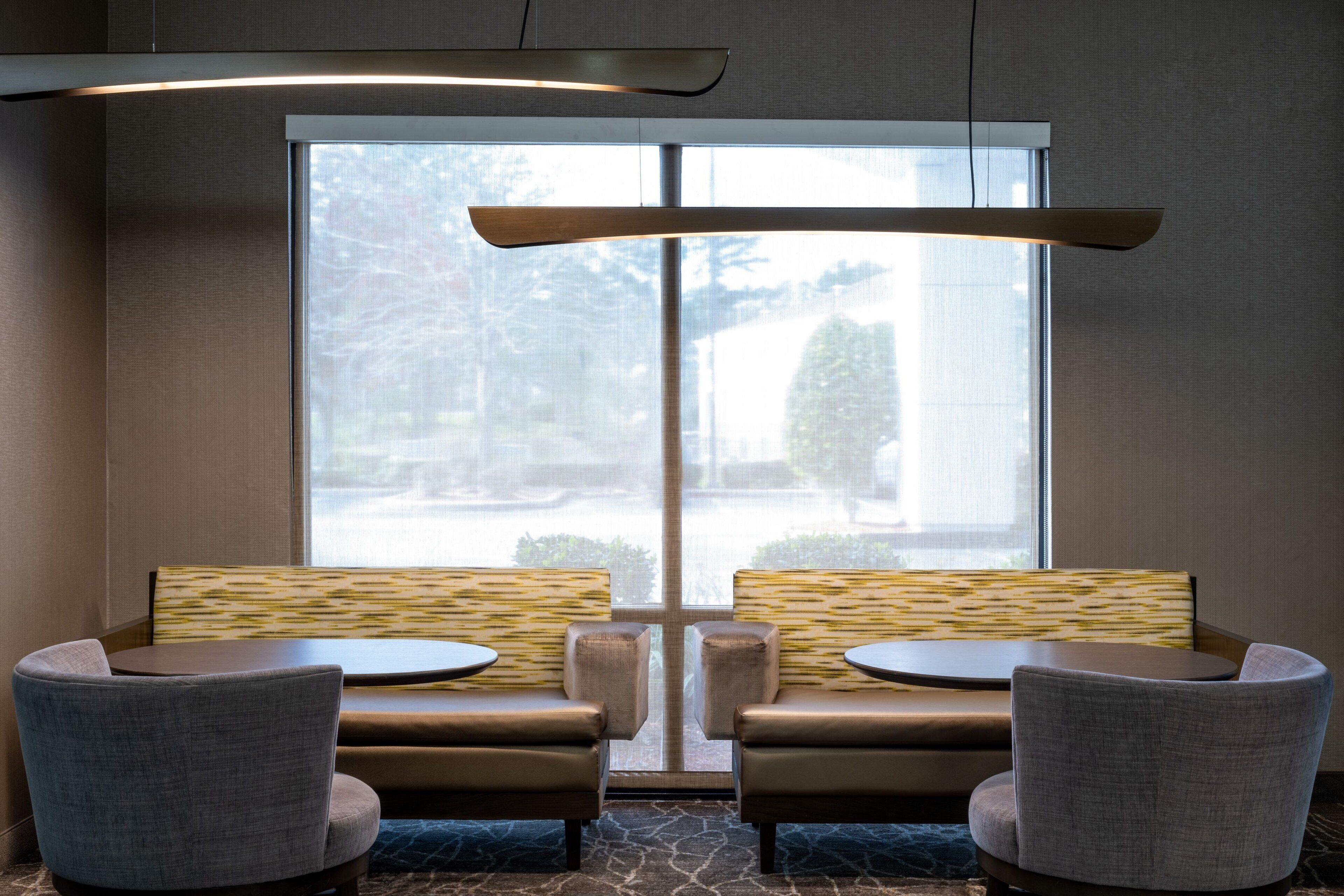 A modern lounge area with a large window, two sofas, and two round tables.