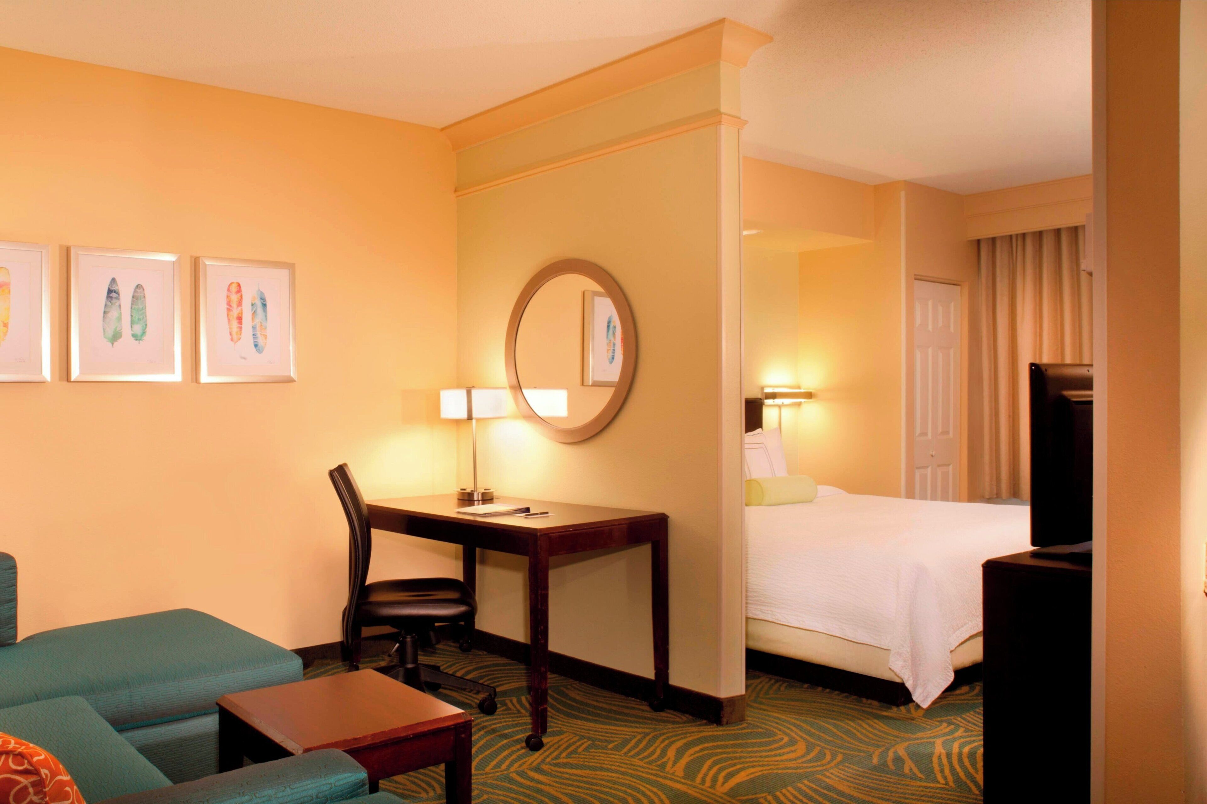 A hotel room with a bed, a desk with a chair, a television, and artwork on the wall.