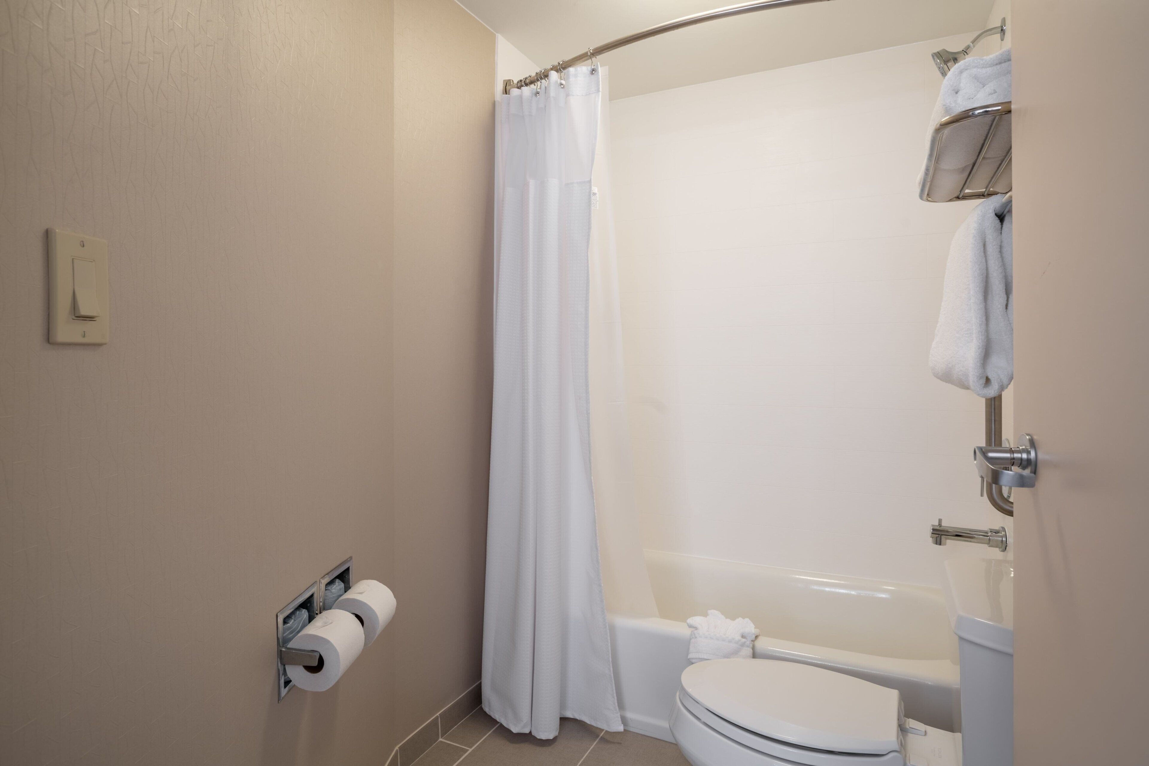 Un baño con inodoro, ducha con cortina, toallero y dispensador de papel higiénico.