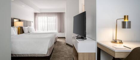 A hotel room with a bed, a desk with a TV, a lamp, and a window with curtains.