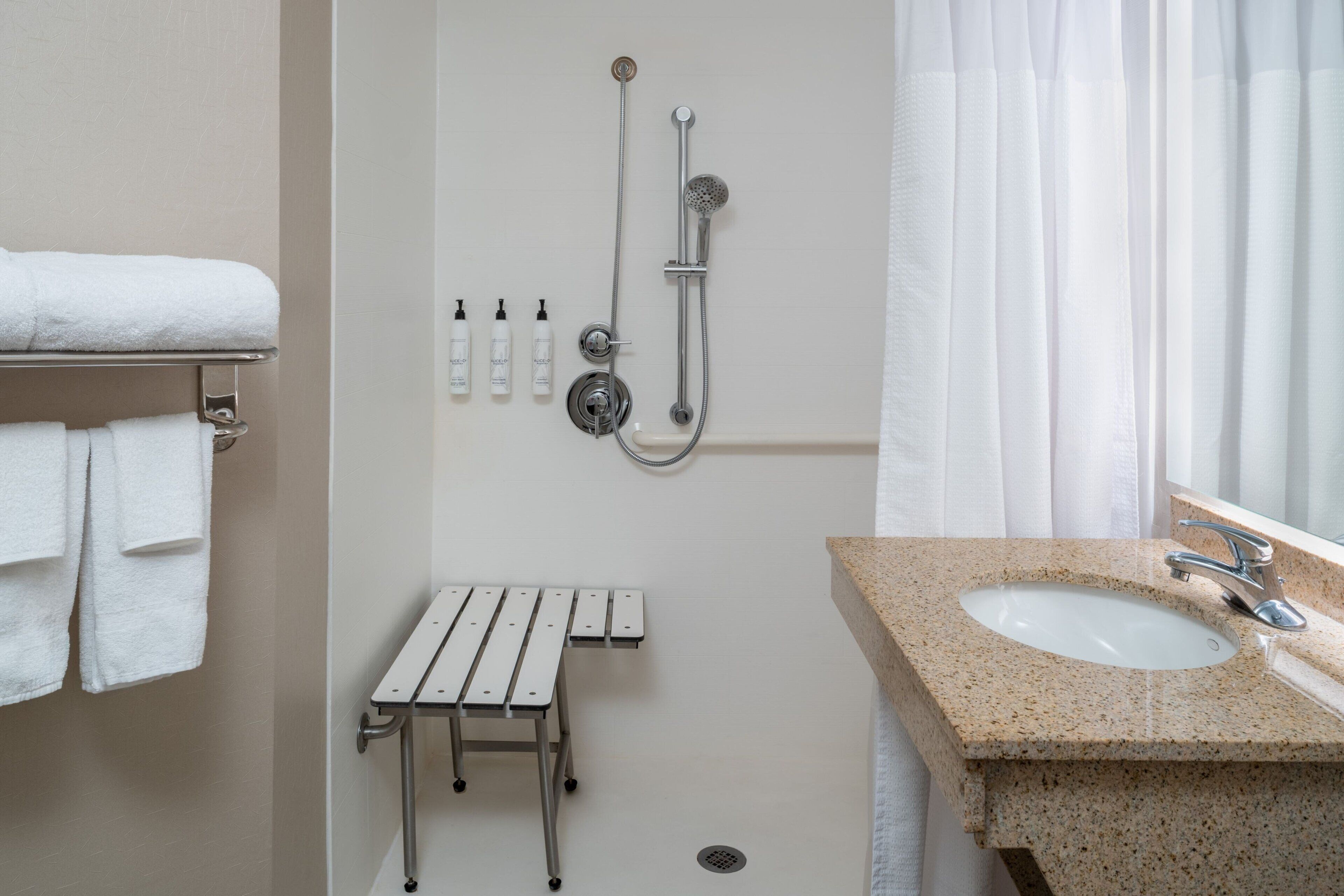 A bathroom with a sink, shower, and a bench.