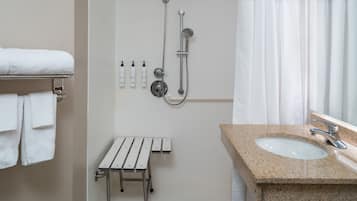 A bathroom with a sink, shower, and a bench.