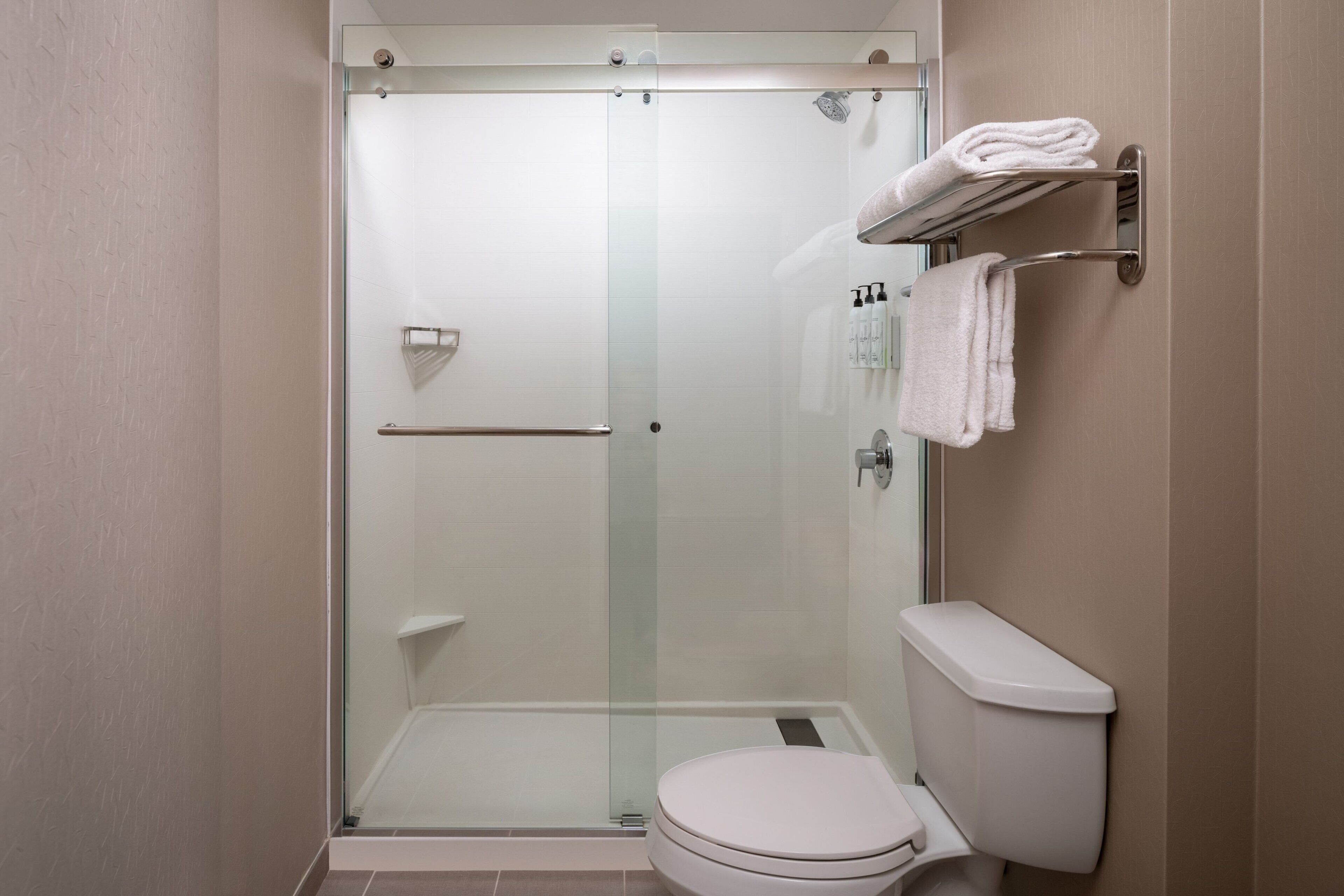 Un baño moderno con ducha de vidrio, un inodoro blanco y un perchero con toallas dobladas.