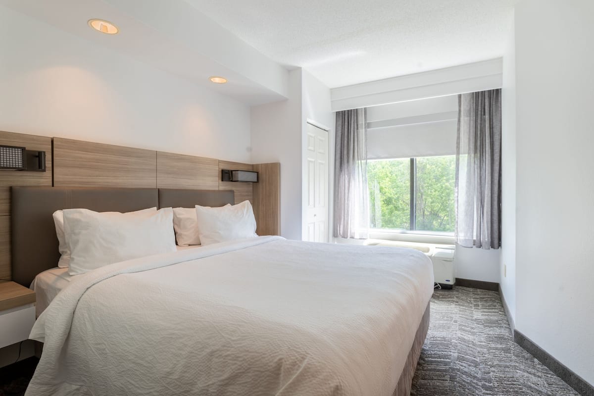 A hotel room with a large bed, a nightstand, a window with curtains, and a ceiling light.