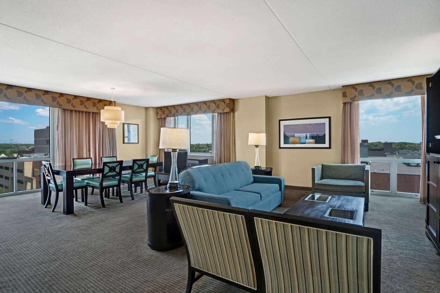 A hotel room with a balcony, a dining area, a sofa, and a television.