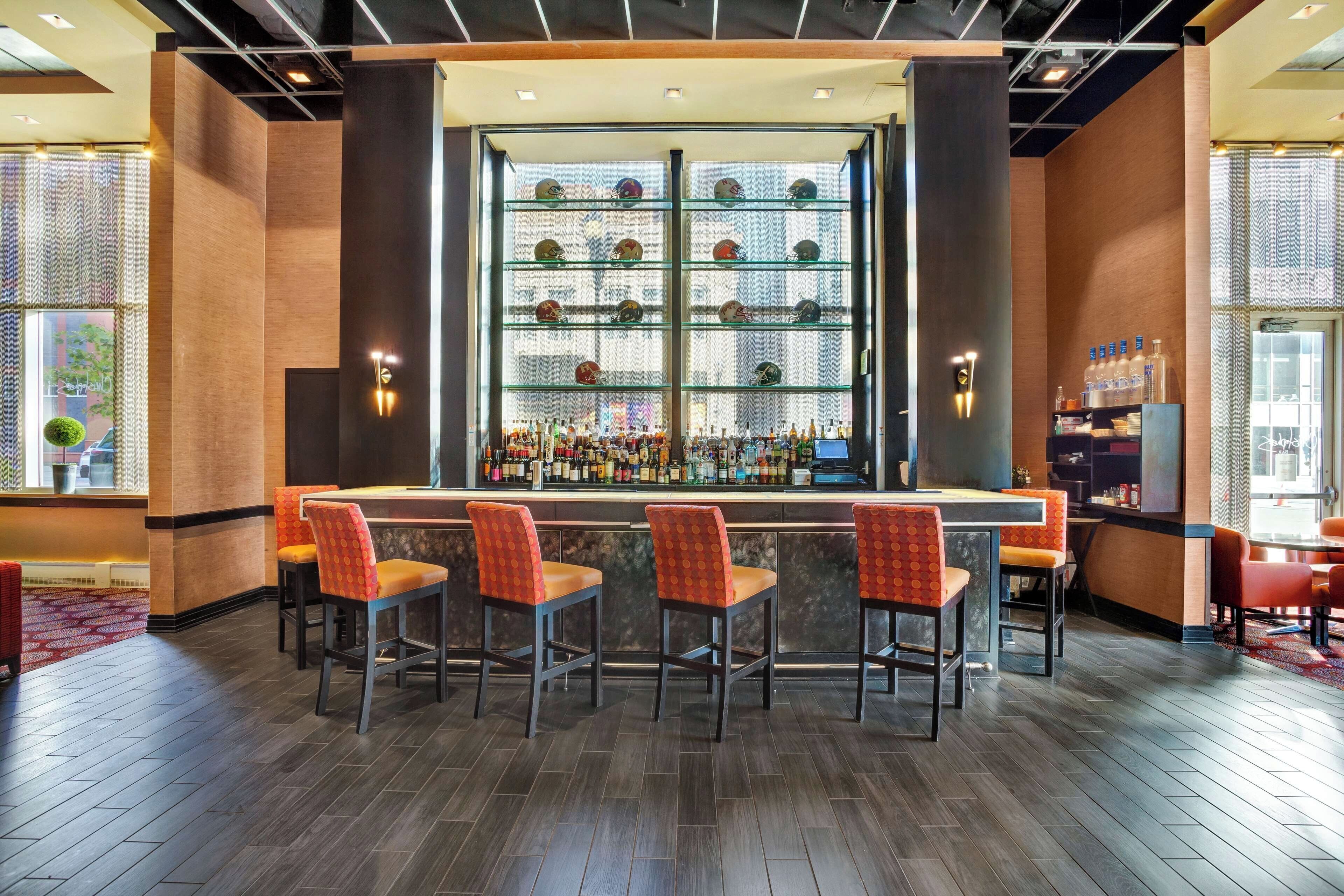 A bar area with a long counter, multiple shelves of bottles, and four bar stools.